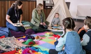Children and adults sitting on the floor with books and musical instruments