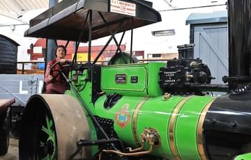 A woman in period clothing driving a vintage steam roller engine