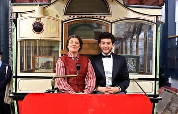 A woman and a man both in period clothing sat on a vintage tram.