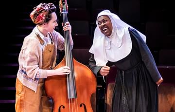 A woman playing a double bass with a nun singing next to her