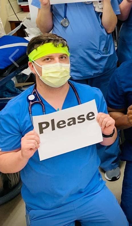 dressed in nursing scrubs and a face mask, josh holds a sign that says "please" dressed in nursing scrubs and a face mask, josh holds a sign that says "please"