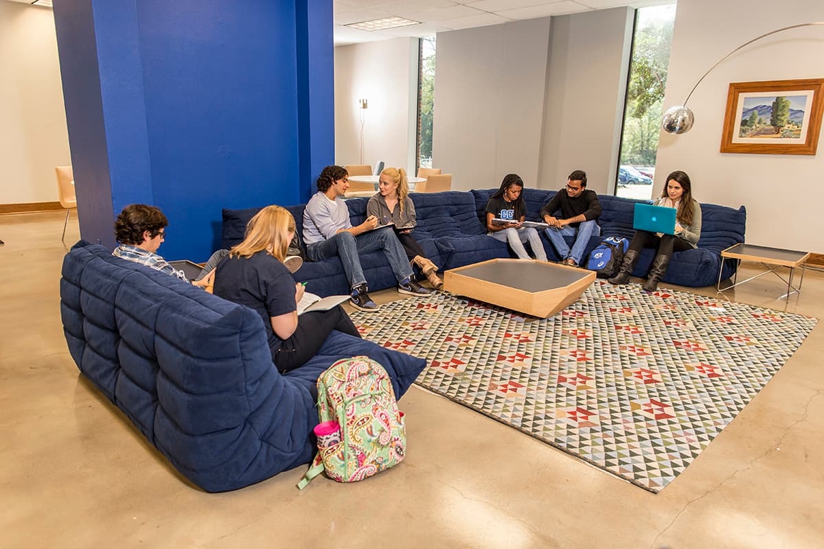 Students sit on a blue U-shaped sofa in the lobby of OCU's Walker Hall dormitory.