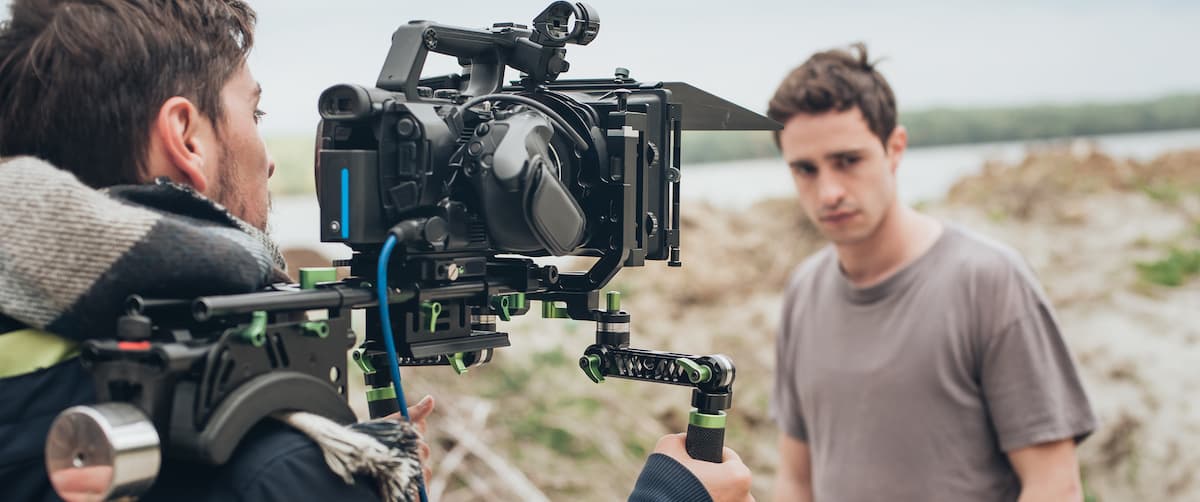 A male actor appears troubled on a beach as a camera operator films him