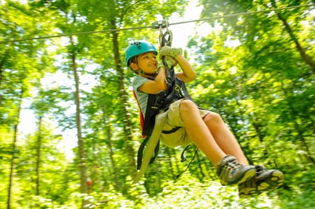 boy zipping on zipline through wooded area