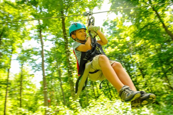 boy zipping on zipline through wooded area