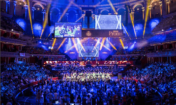 An orchestra on stage at the Royal Albert Hall with a large audience watching.