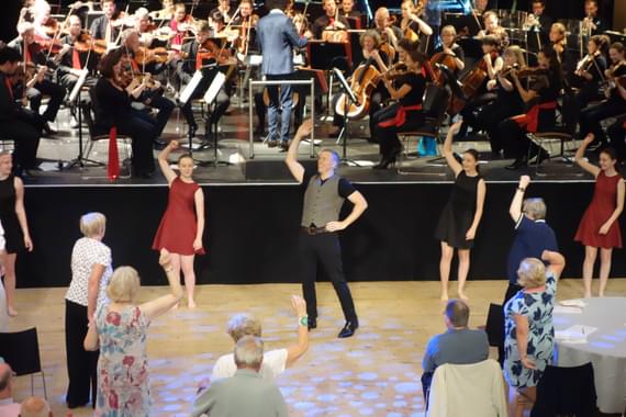 People dancing in front of an orchestra on a stage.