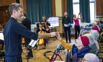 Orchestra conductor holds the hand of an elderly lady in the audience.
