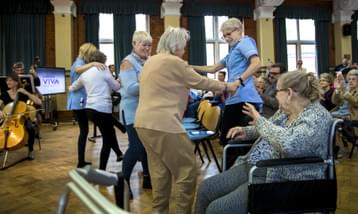 Care home staff and residents dancing in front of an orchestra.