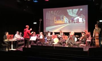 A group of musicians performing in front of a screen showing a film.