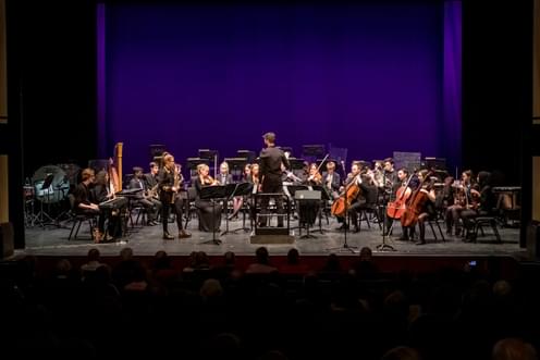 An orchestra on stage made up of participants and professional musicians, with a saxophone soloist at the front.