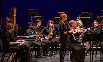 A solo saxophone player in front of an orchestra of students and professional players