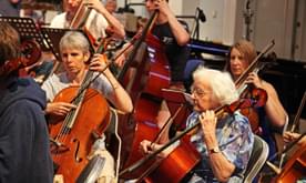 An older woman playing cello in an orchestra,