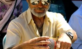 An older man in a hat and sunglasses playing a percussion instrument.