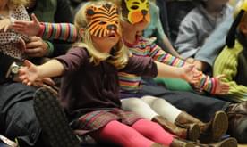 Two young girls with animals masks sat on the floor gesturing with their arms open.