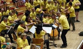 A mid-short of a large group of musicians on stage, all in yellow t-shirts.