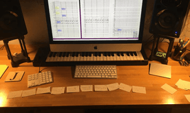 A desk with a computer, a musical keyboard, and lots of paper notes