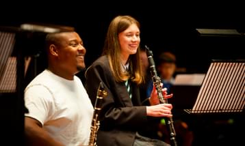 A black man with a clarinet sits next to a white girl with a clarinet, both are smiling