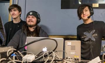 Three boys sat at a technical sound desk, two wear a microphone headset..