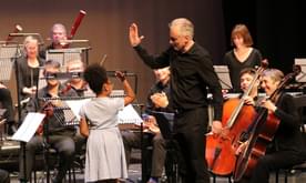 A young girl on stage receiving a high-five from the conductor