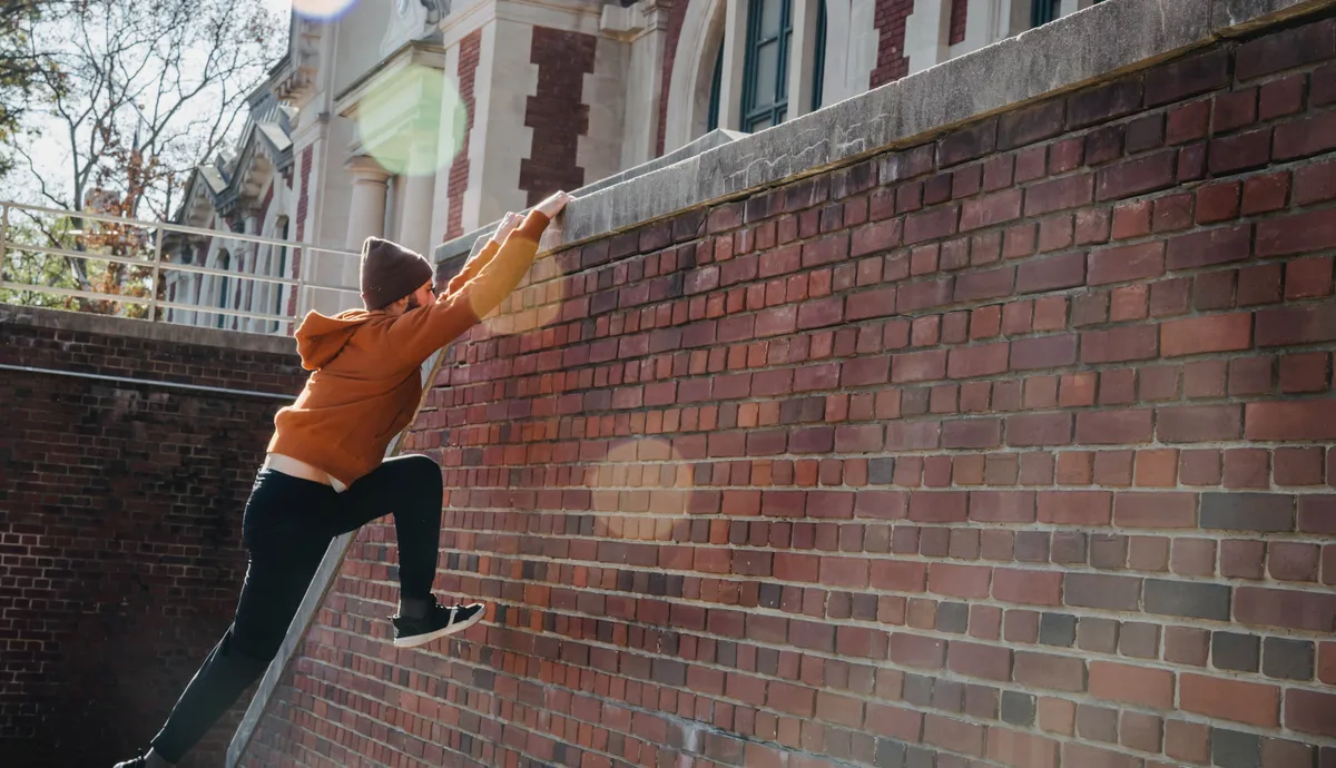 Man in orange hoodie jumping over wall