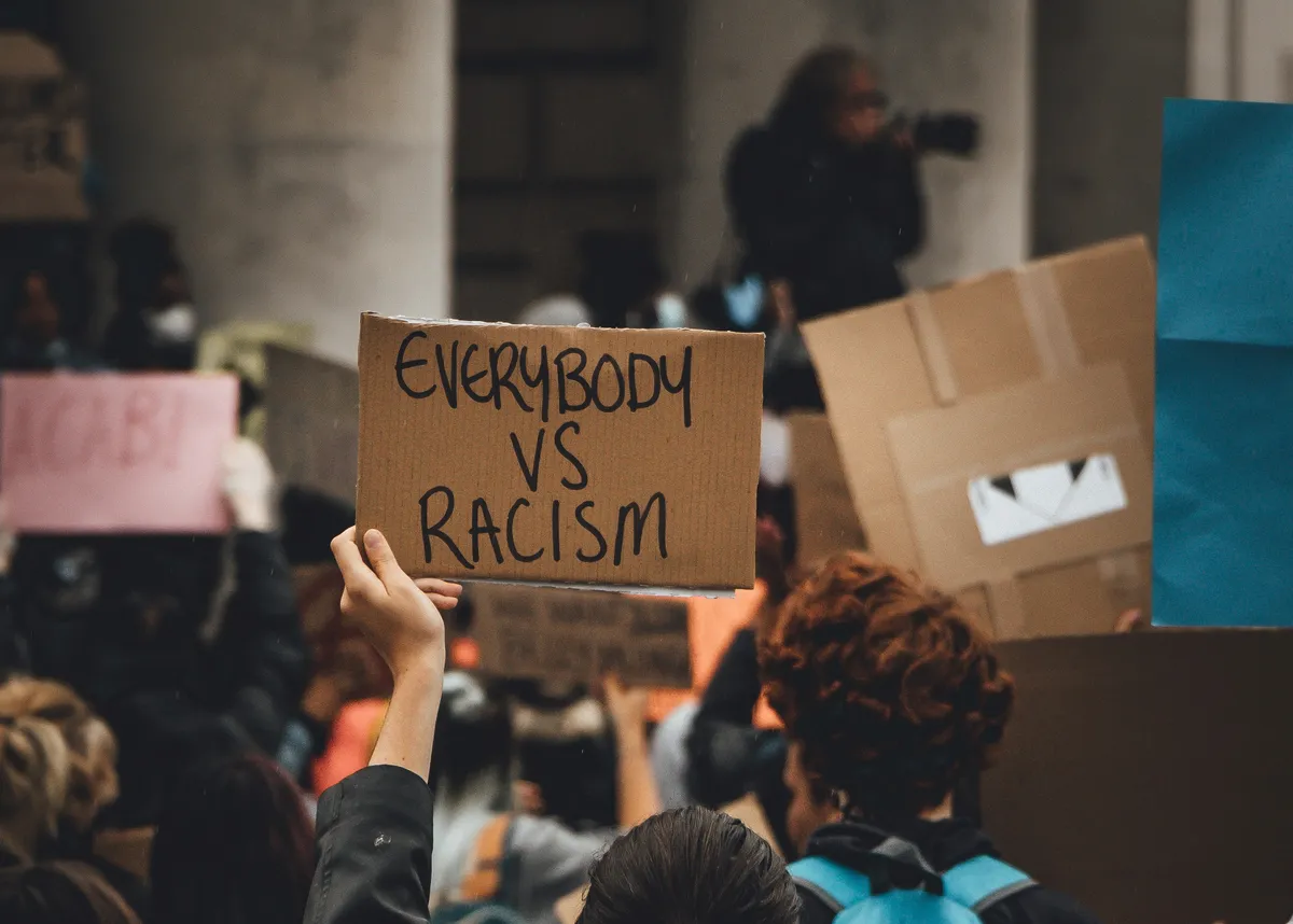 A person holding a cardboard sign with 'everybody vs racism' written on it