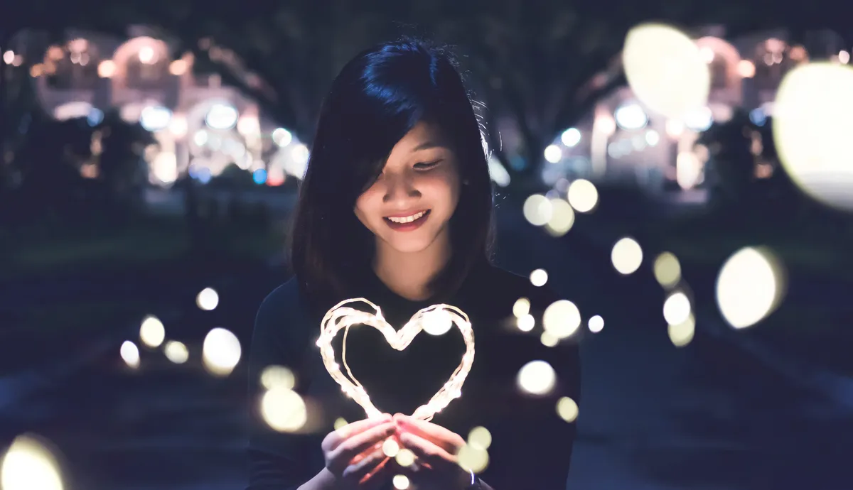 Woman with black hair surrounded by lights and holding a some lights in the shape of a heart
