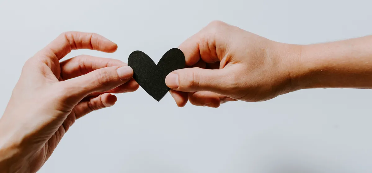 Two hands holding a small black paper  heart