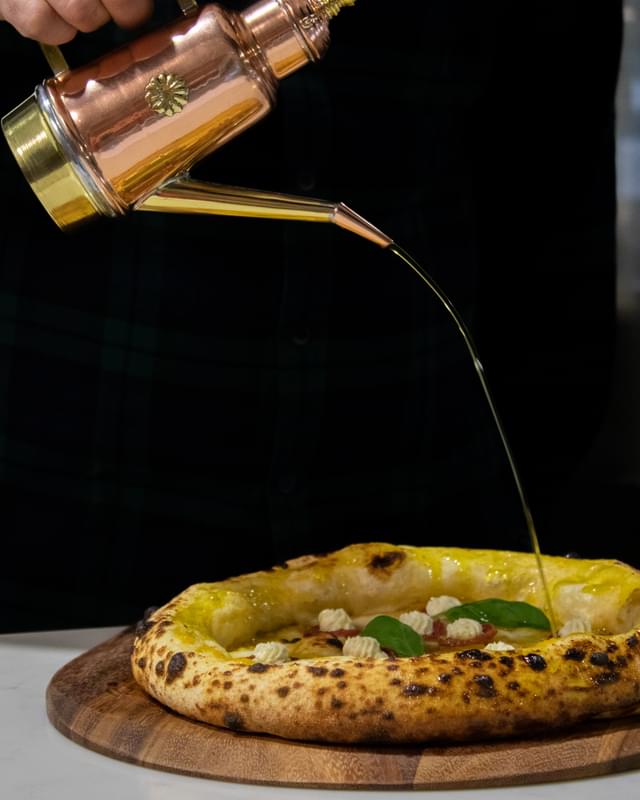 A man pouring olive oil onto a pizza.