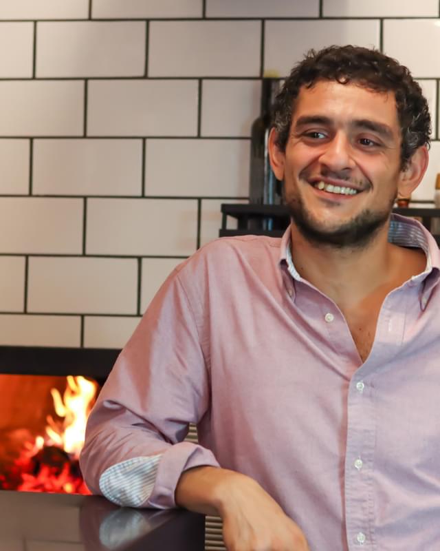 A man smiling in front of a fireplace.
