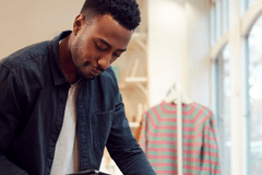 Black man in a dark blue long-sleeve shirt in a retail store holding a tablet while working.