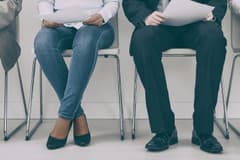 A row of seated job candidates. There are two men, and two women. The picture is cropped below their feet and at their ribcage, so the faces are not visible.