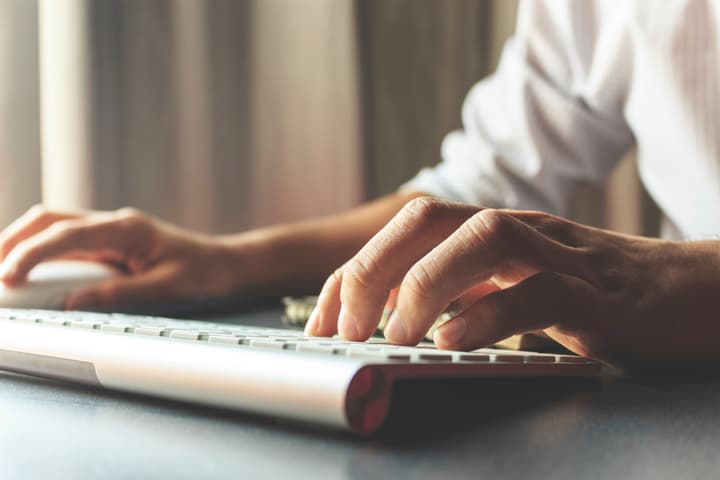 An older business man's hands type on a wireless keyboard.