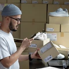 Asian male uses a mobile app on a smartphone to check the product information on a package he is preparing for shipment.