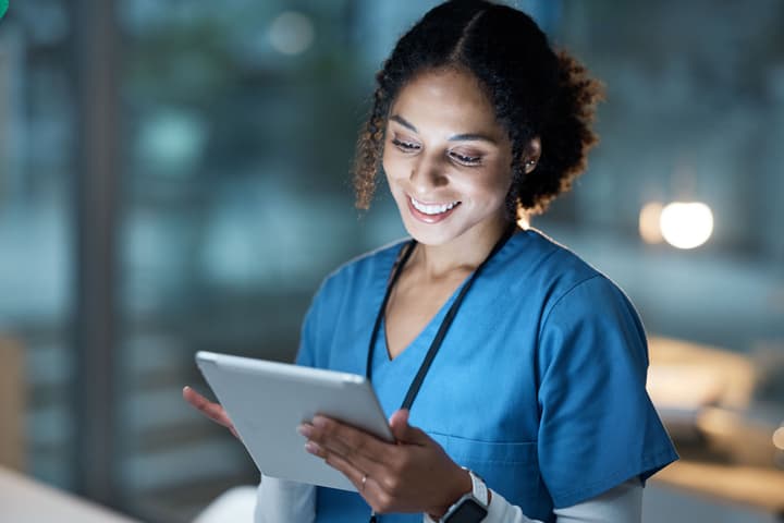 A young black female healthcare provider smiles while looking at a tablet.