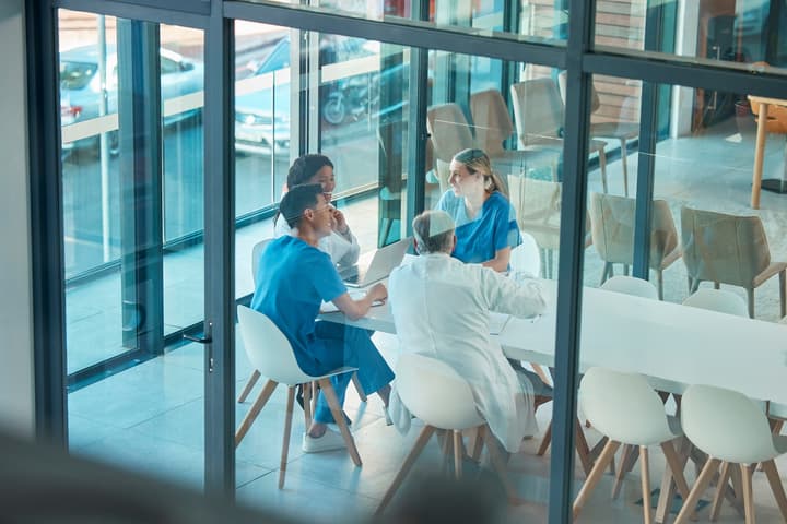 A view from through a window of a group of healthcare providers siting at a table having a meeting.