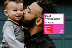 A father with glasses holds a toddler and is kissing his cheek with a Great Place to Work Best Workplaces for Parents 2022 badge overlaid.