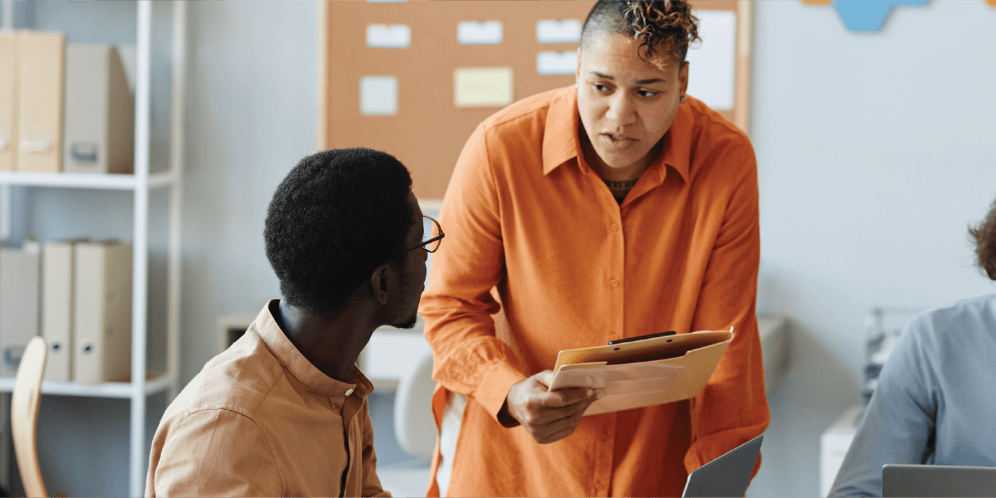 Business people in a workspace communicating and looking at computers and documents.