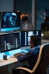 Man sits at a desk with three computer monitors working