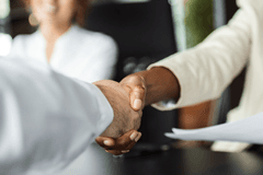 Close up image of two business people shaking hands. One is a white man, the other is a Black woman.