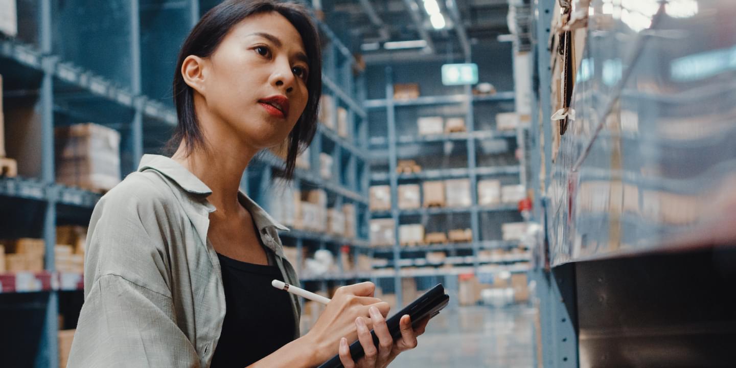 A female in a warehouse looking at shelves while taking notes.