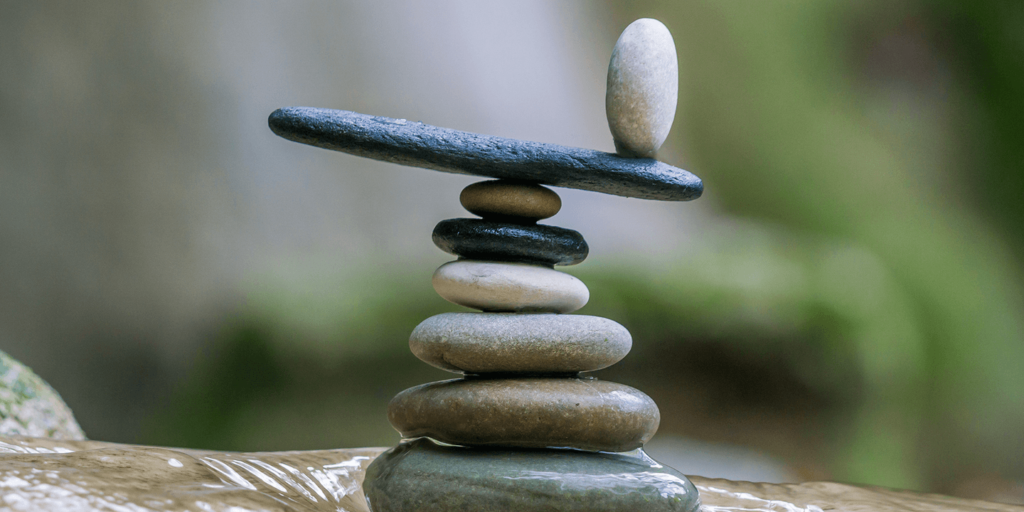 A cairn of smooth river stones are stacked on top of one another. One stone at the top has been turned to balance on its short end.
