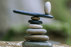 A cairn of smooth river stones are stacked on top of one another. One stone at the top has been turned to balance on its short end.