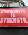 Photo of a large, red sign on the side of a building that reads "Community is Strength." Photo by John Cameron via Unsplash.