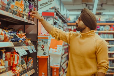 An young Indian man wearing a yellow turtleneck sweater and a brown turban shops for food in a supermarket. Photo by Dollar Gill via Unsplash.