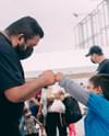 A Hispanic man fist bumps a Hispanic child. They are both wearing face masks. Photo by Claudia Raya via Unsplash.