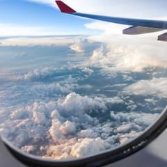 The view outside of an airplane window with a view of the wing of the airplane and sky and clouds
