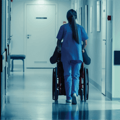 A healthcare worker batting burnout pushes a wheelchair in a hospital