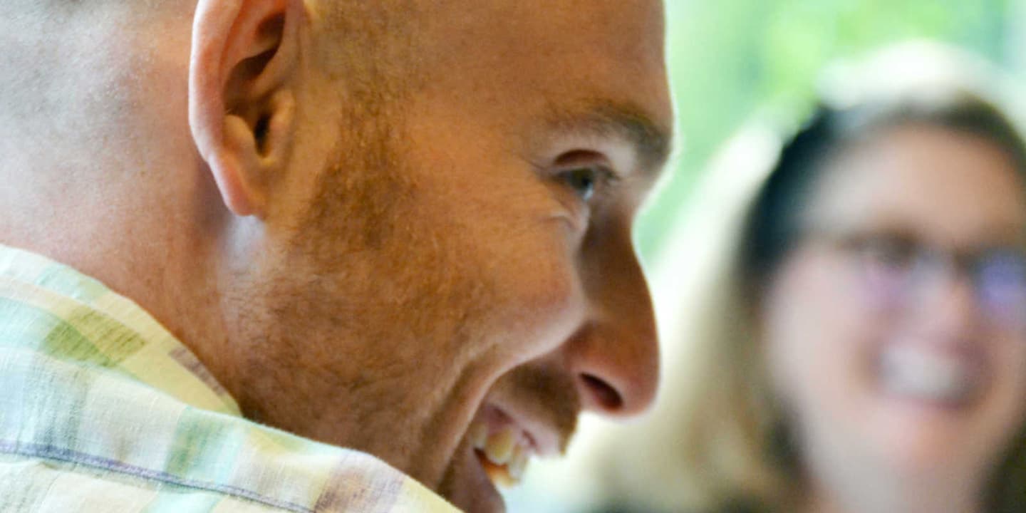 A close up of Propellerite Riley Smith's face in profile. In the background, the image is blurry, but fellow Propellerite Kerri Evans is visible.
