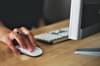 Close up of a white woman's hand using a wireless mouse next to a desktop computer and wireless keyboard. Photo by Vojtech Okenka via Pexels.com